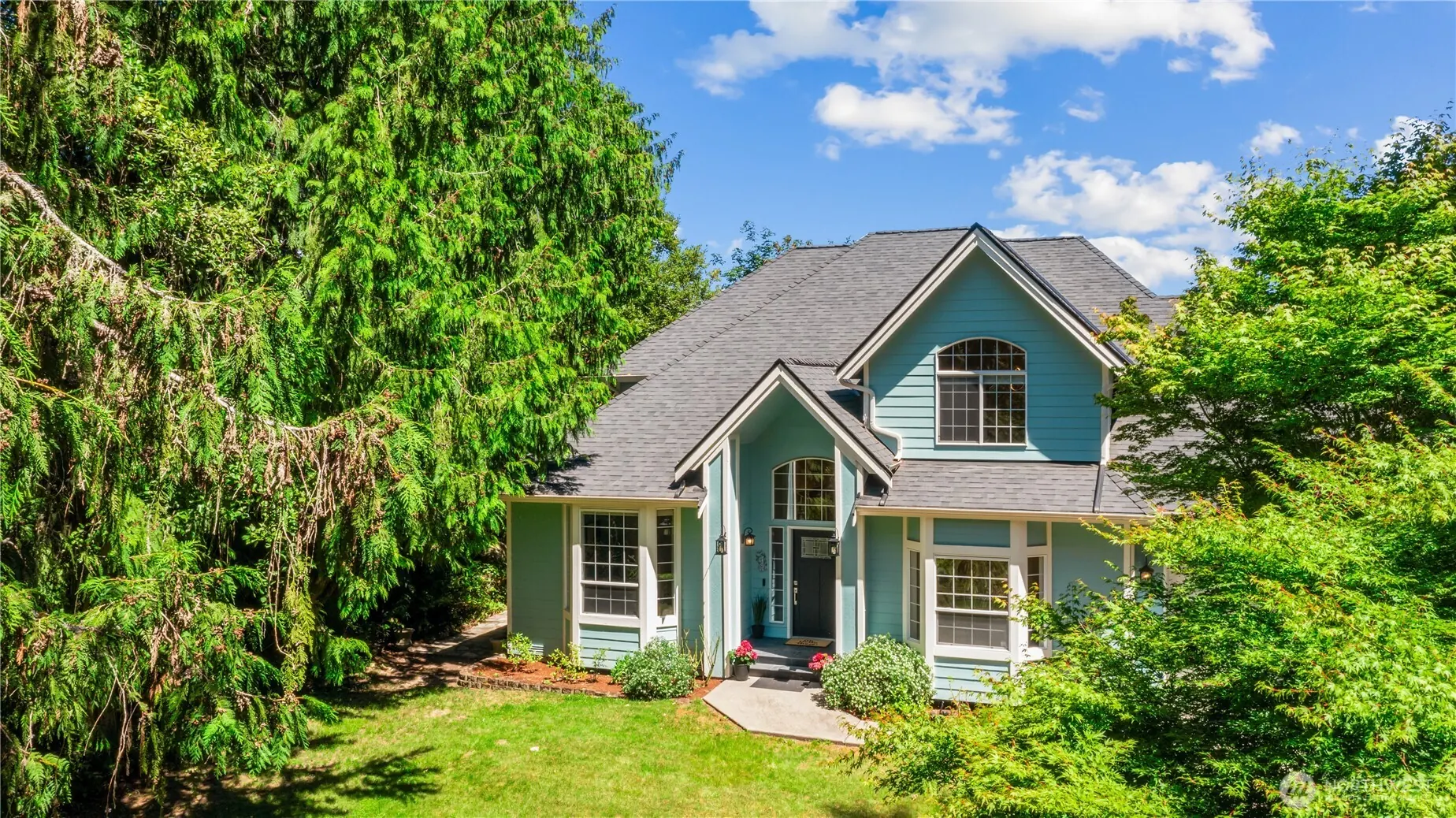 The same turquoise house seen through tall evergreens at the end of its lawn, in full colour.
