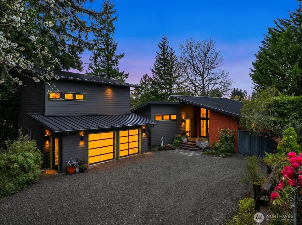 Modern dark-sided home with glowing windows and metal roofs at dusk.